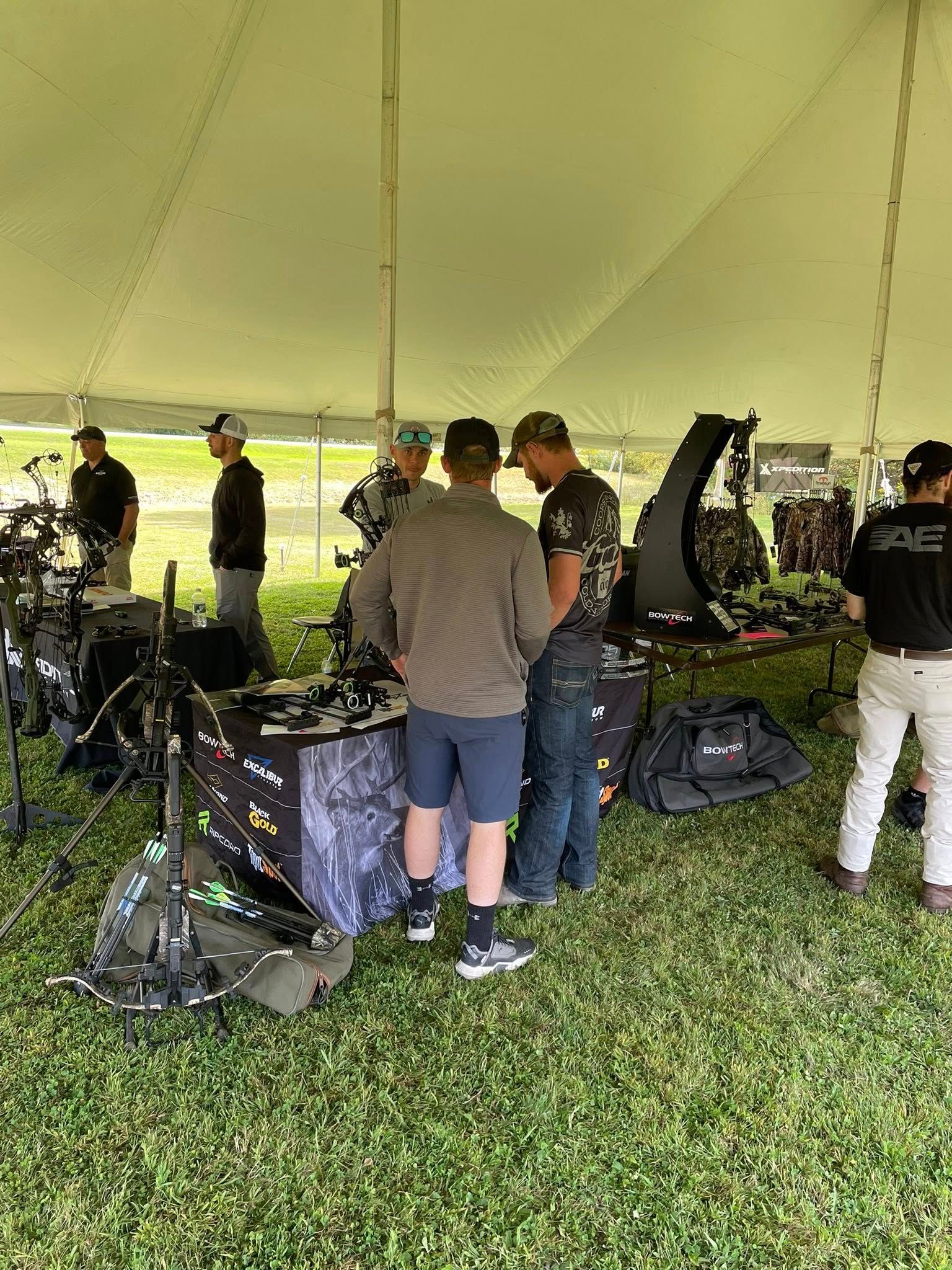 People examining outdoor gear at a booth under a tent, possibly at a sporting event.