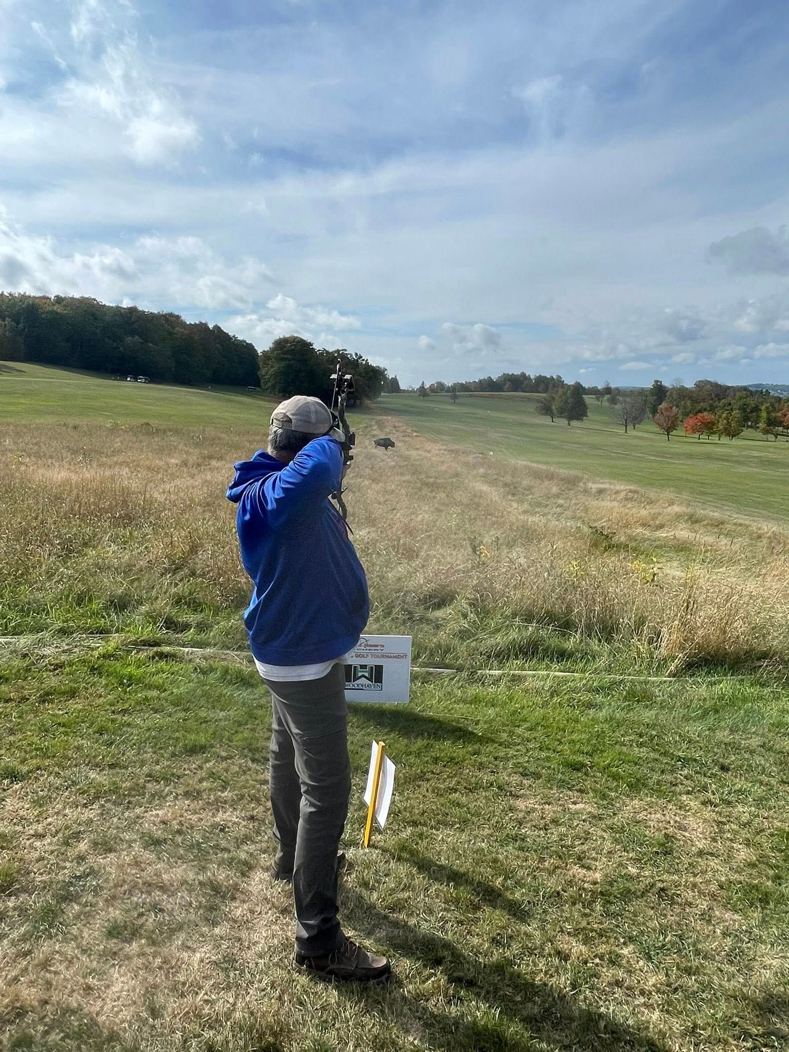 Person shooting a bow and arrow at an archery range on a sunny day.