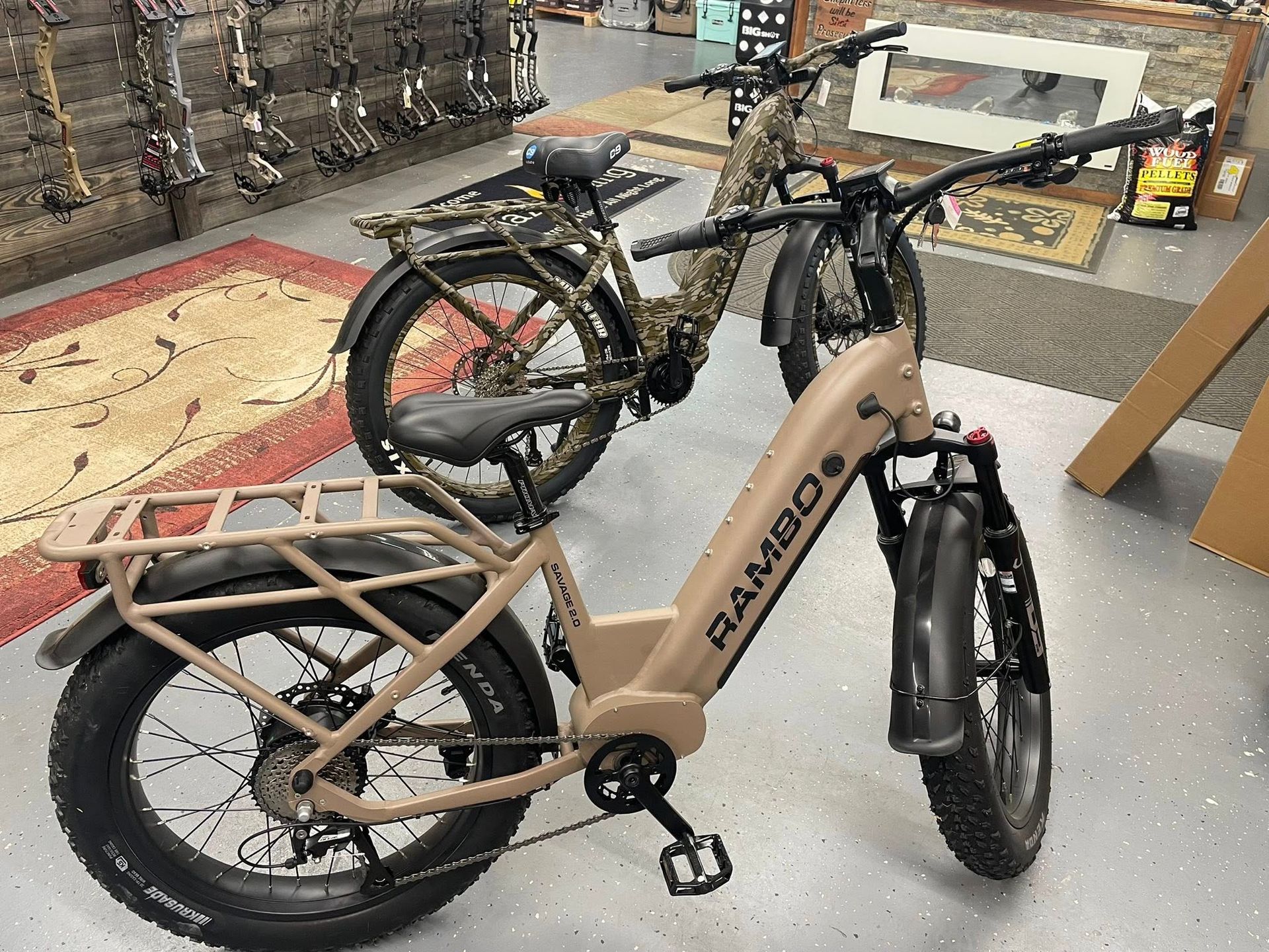 Two tan and camouflage Rambo electric bikes inside a store, one in focus.