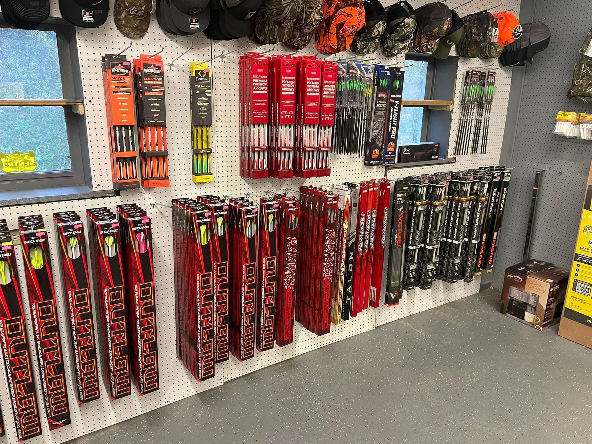 Hunting gear display in a store, including arrows, hats, and other equipment on a wall.