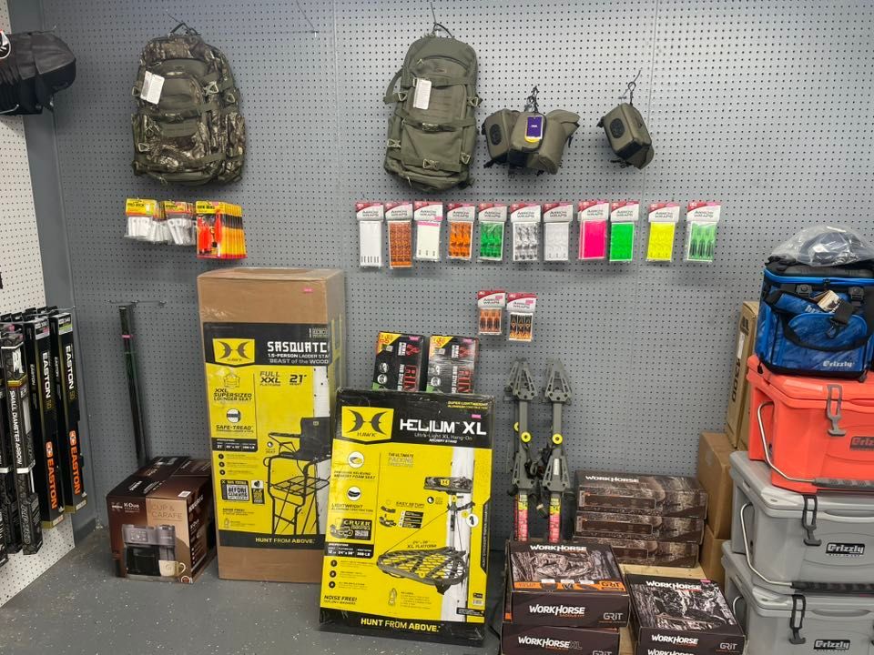 Shelves displaying outdoor gear: backpacks, tackle boxes, fishing rods, and accessories, against a gray wall.