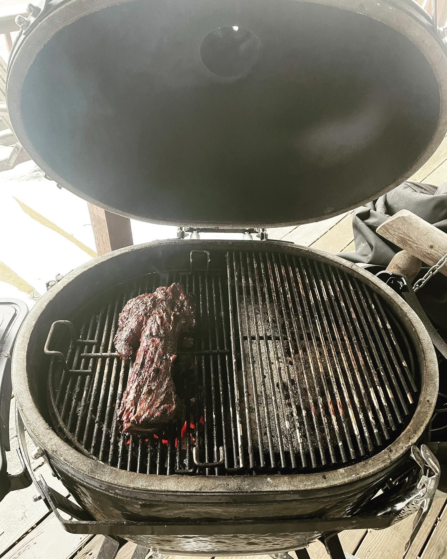 A large, open grill with a piece of meat cooking on the grates. The grill is outdoors.