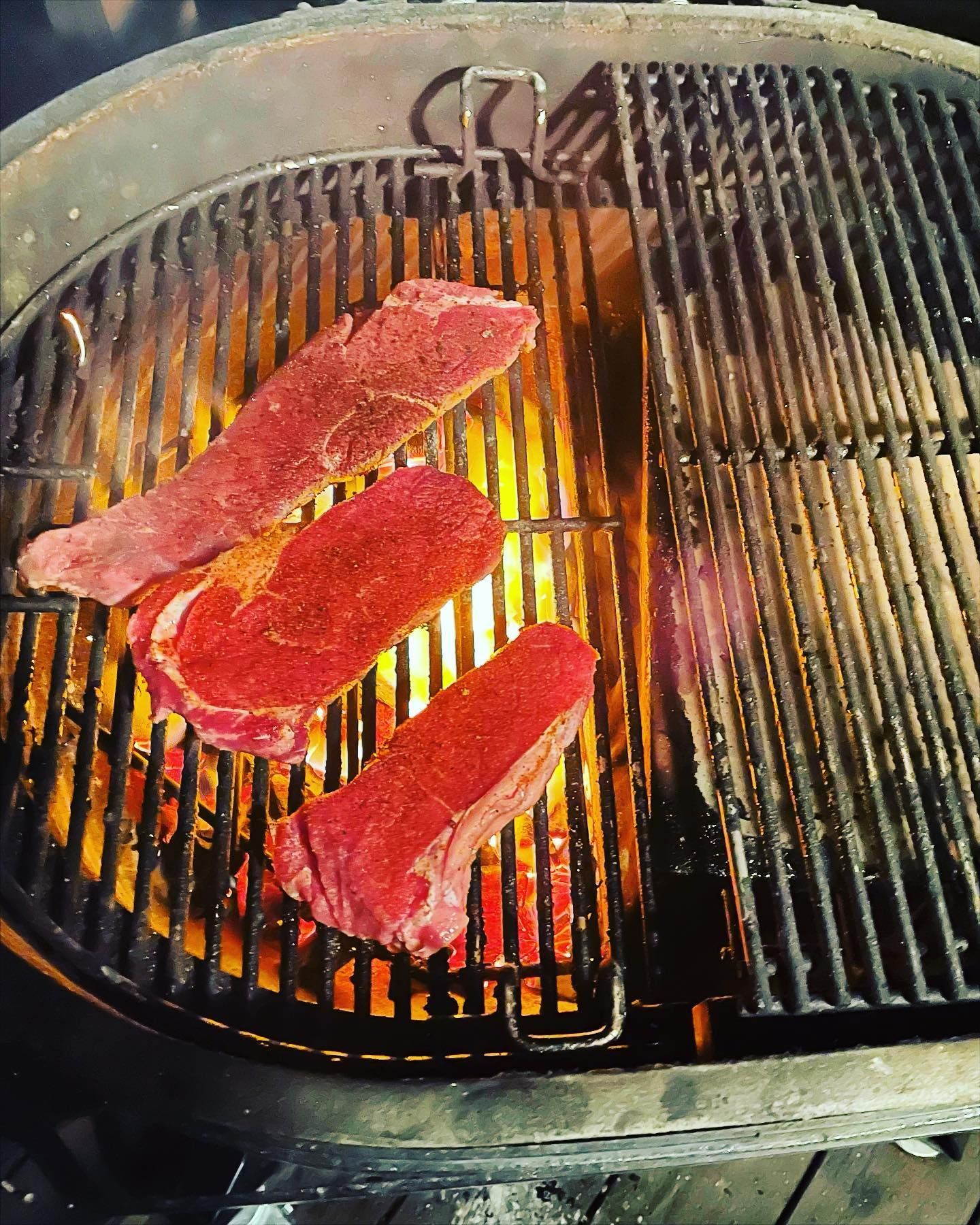 Steaks grilling on a hot barbecue with visible flames.