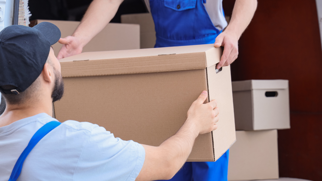 Two people in work clothes loading a cardboard box into a truck.