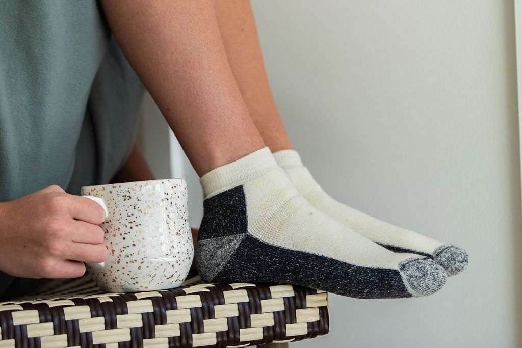 Person relaxing, wearing socks, with a coffee mug in their hand.