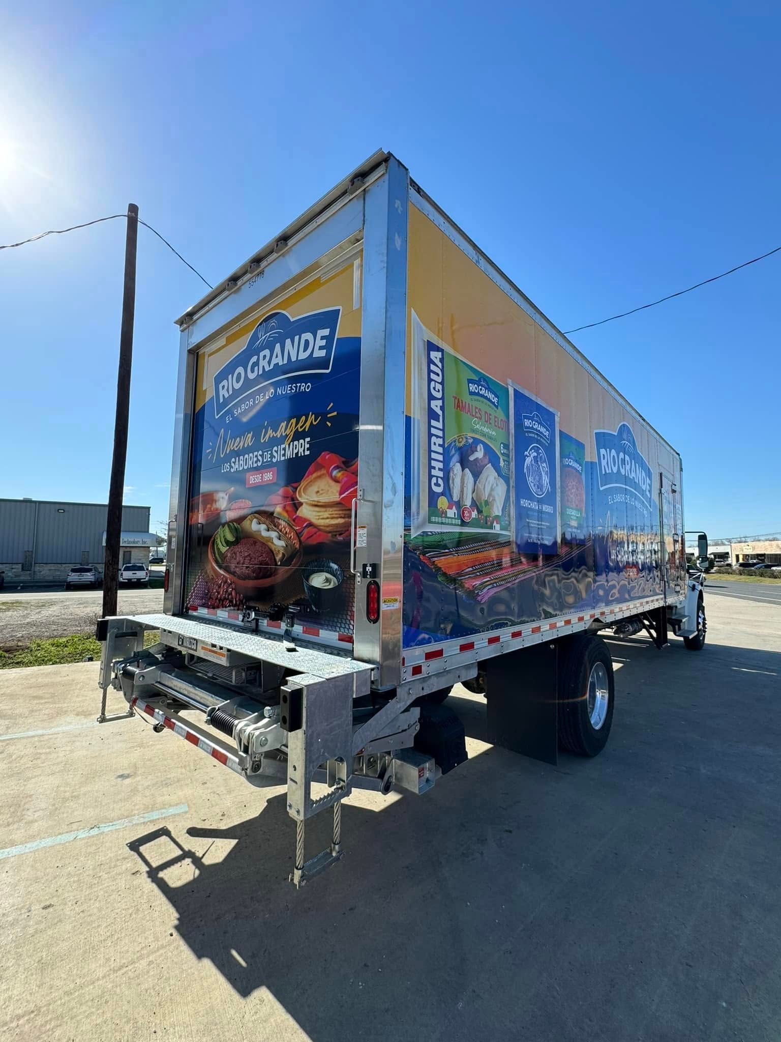 A side and rear view of a commercial delivery truck parked in a lot, featuring colorful food-themed graphics.