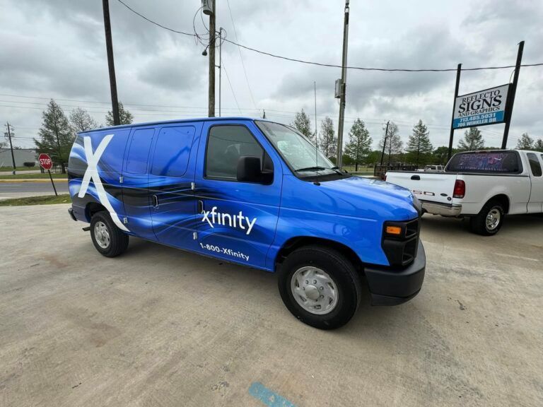 A blue Xfinity-branded work van parked on a concrete lot next to a white pickup truck.