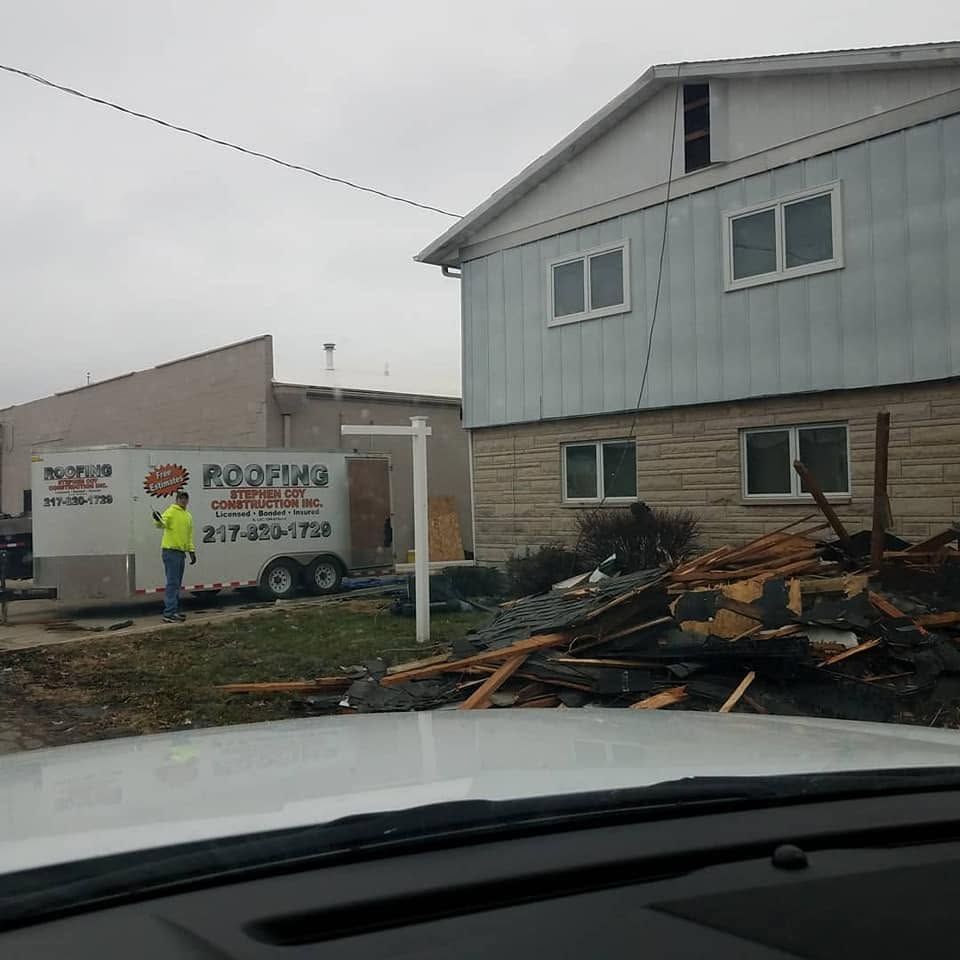 Storm damage cleanup at a house, with debris piled in front and a worker by a truck in the driveway.