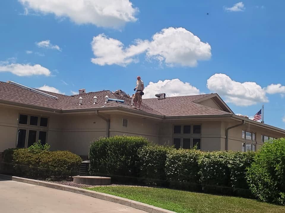 Person on a roof of a beige building under a blue sky with clouds