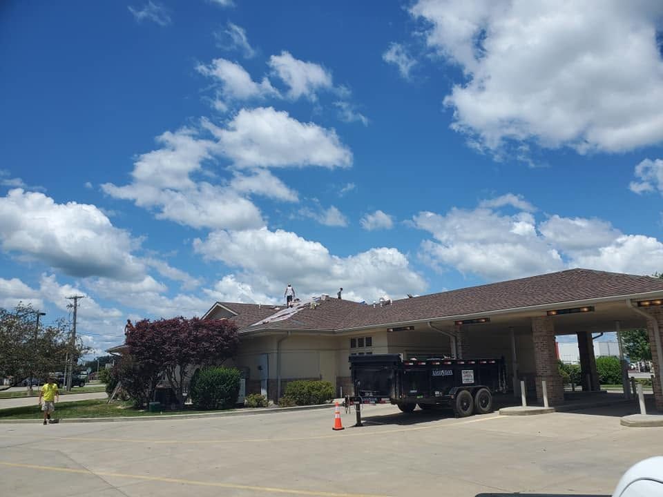 Single-story building with covered entrance, parked utility trailer, and a partly cloudy blue sky
