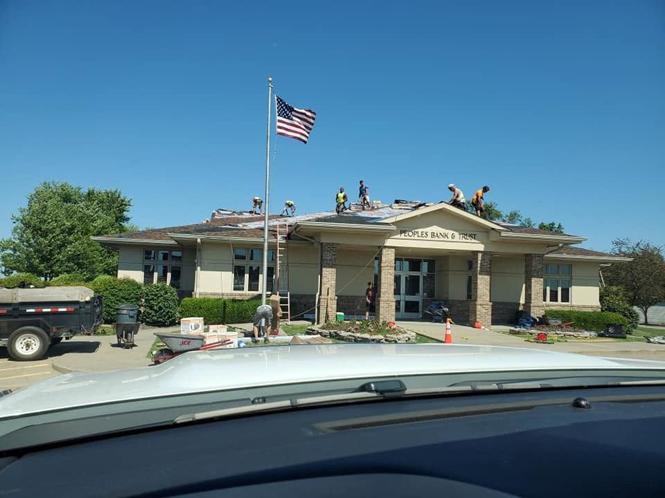 Low building with people on the roof, U.S. flag flying, seen from a car windshield on a sunny day