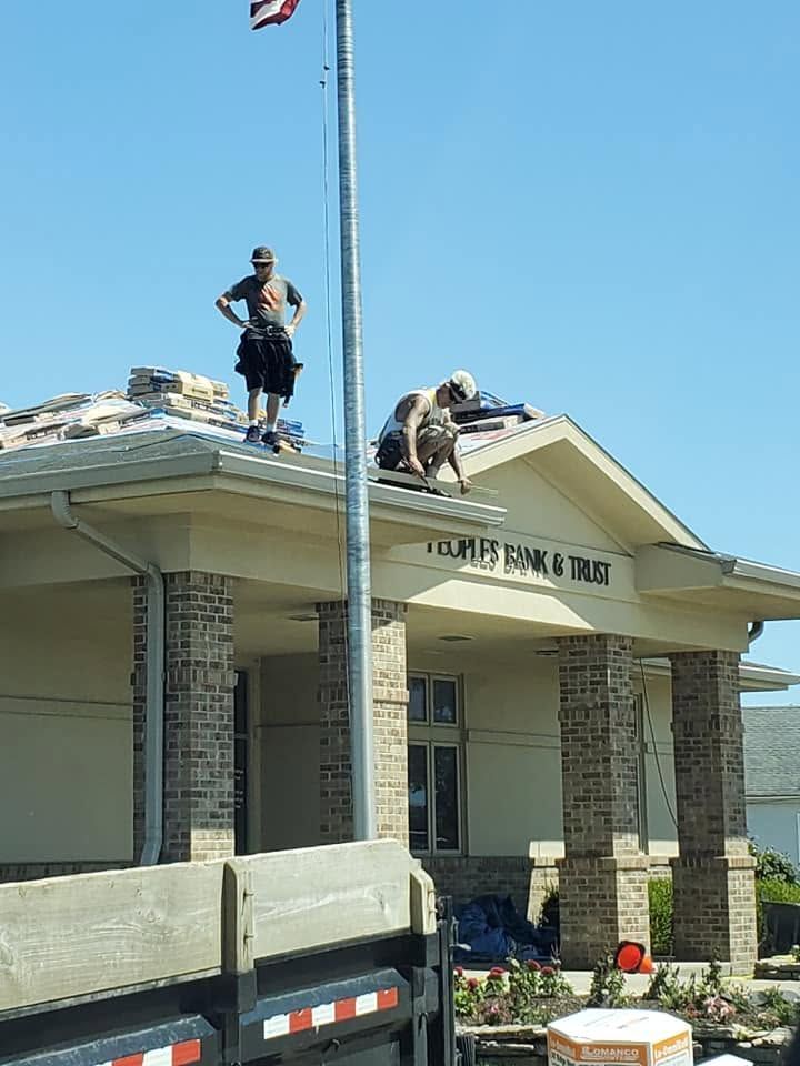 Workers on a building roof near a flagpole, repairing the edge above an entrance.