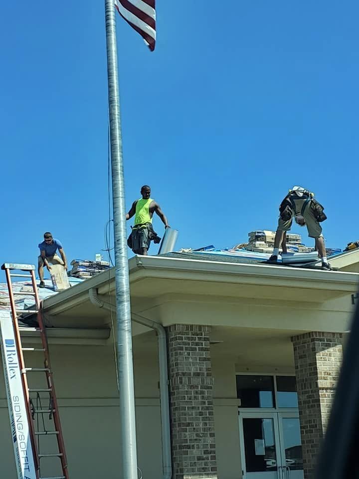 Workers repairing a building roof under a blue sky, with an American flag on a pole nearby