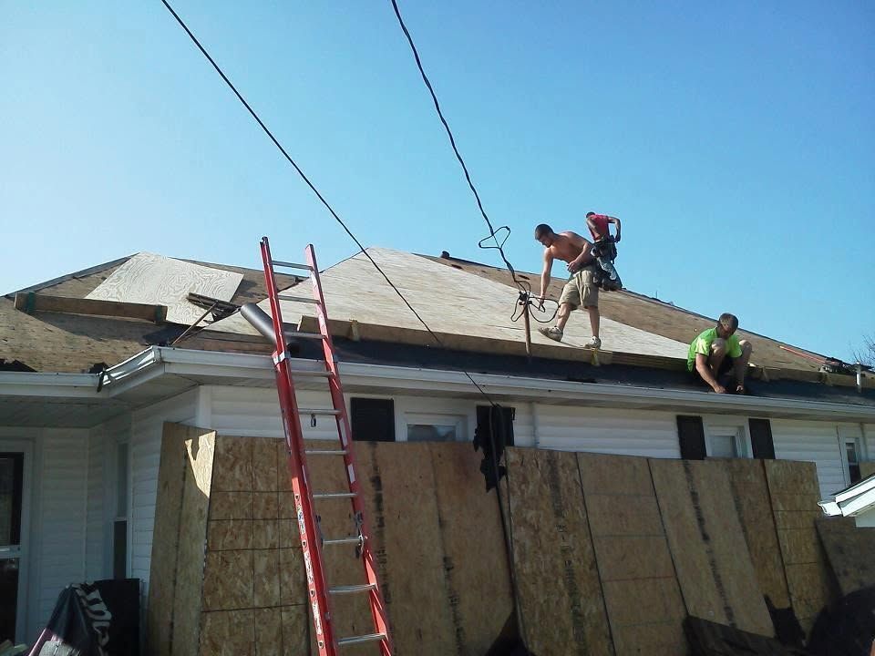 Workers repairing a roof on a house, with one on a red ladder and another on the rooftop.