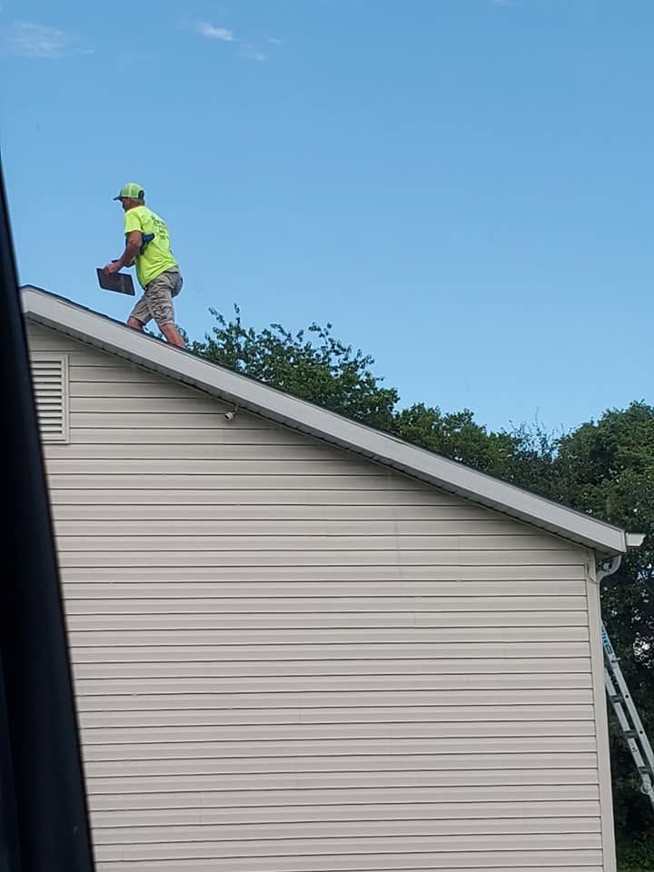 Worker in neon safety gear on a rooftop, carrying a tool against a blue sky.