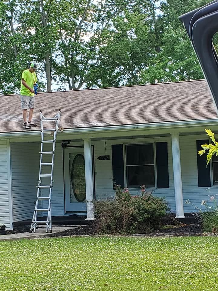 Worker on a roof beside a ladder, inspecting or repairing a light-blue house.