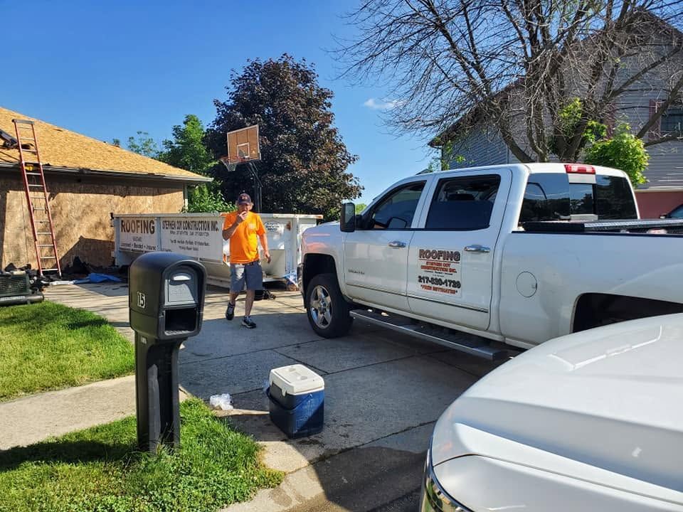 Worker beside white pickup truck at a residential driveway with yard signs and a mailbox
