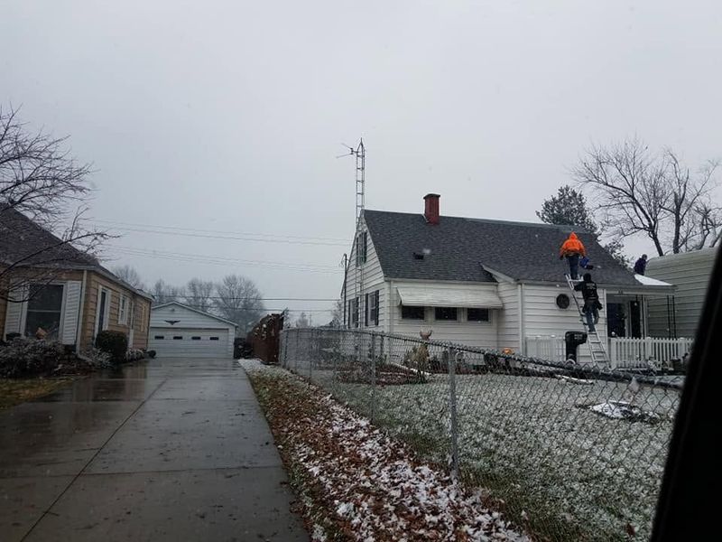 Snow-dusted suburban driveway beside a white house with an orange traffic cone on the roof and overcast sky