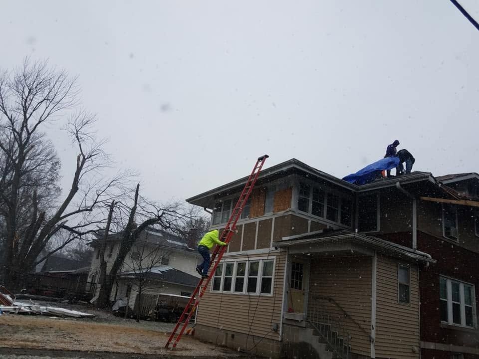 Workers on a roof and ladder repairing a two-story house in winter under cloudy skies