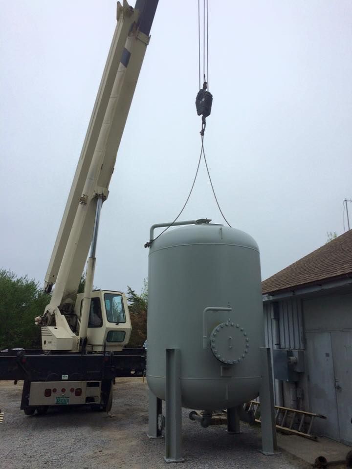 A large crane rented from Mayo Crane Rental lifts a steel tank