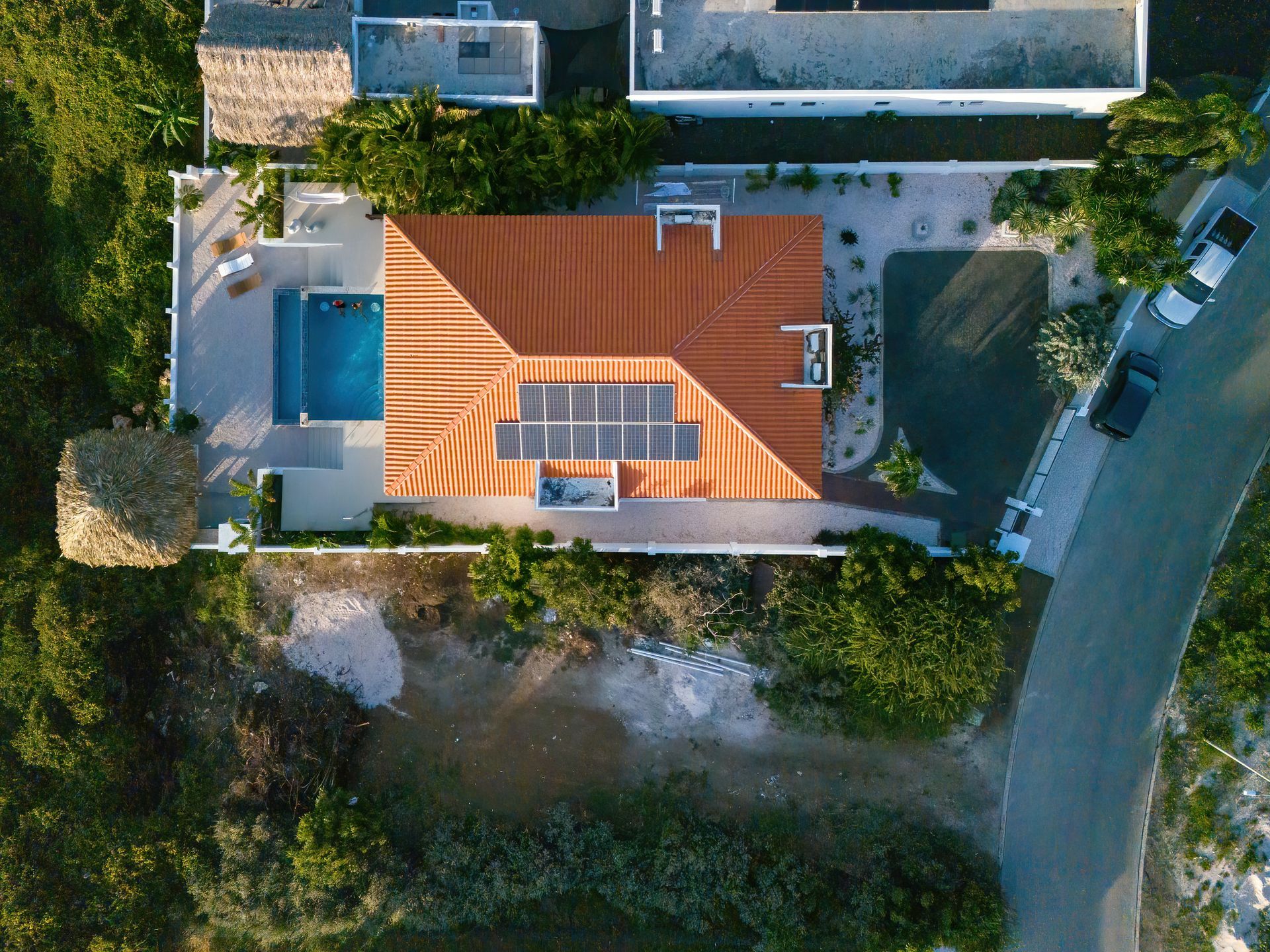 Luchtfoto van een huis met een zwembad, zonnepanelen en een bruin pannendak; een verharde oprit en weg zijn zichtbaar.