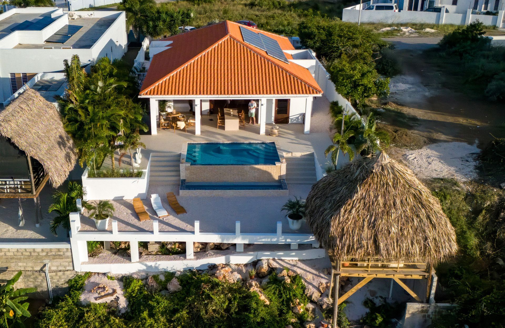 Tropische villa met zwembad, twee rieten hutten en een oranje pannendak.