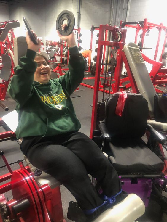 A woman is sitting on a machine in a gym holding a barbell.