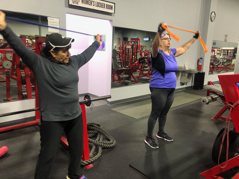Two women are doing stretching exercises in a gym