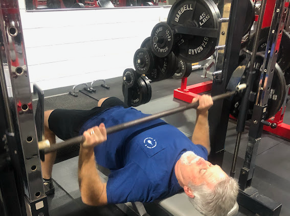 A man is laying on a bench lifting a barbell in a gym.