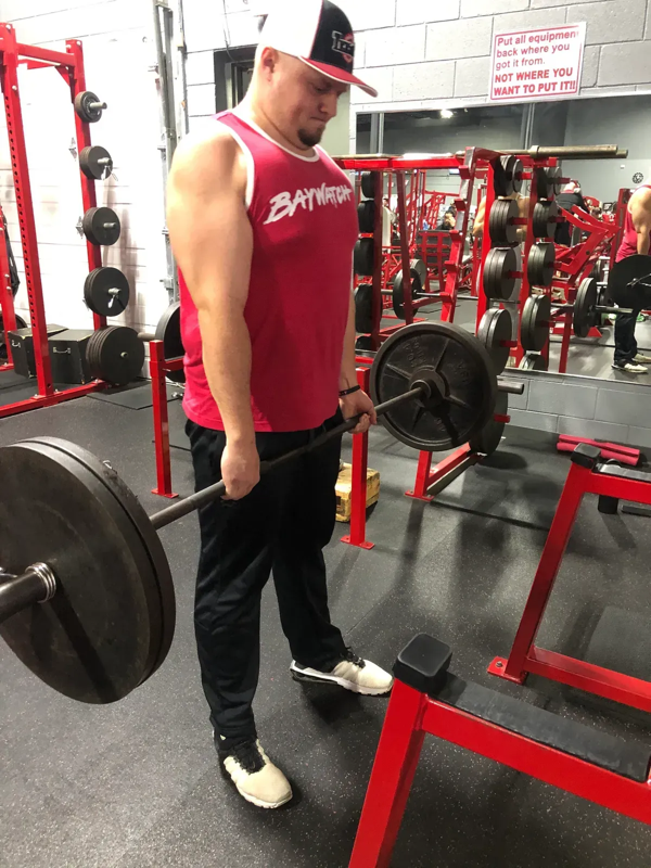 A man in a pink tank top is lifting a barbell in a gym