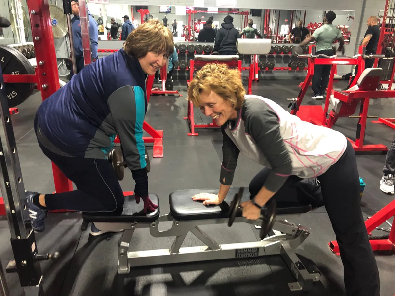 Two women are squatting on a bench in a gym