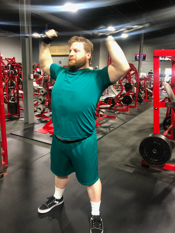 A man in a green shirt is lifting a barbell in a gym