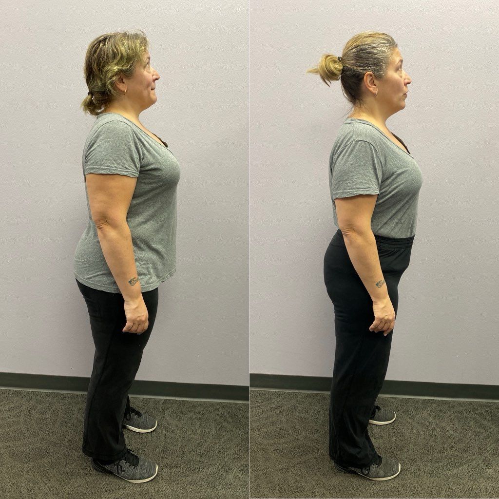 A woman in a grey shirt and black pants is standing in front of a wall.