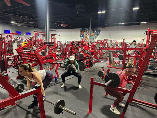 A group of people are squatting with barbells in a gym.