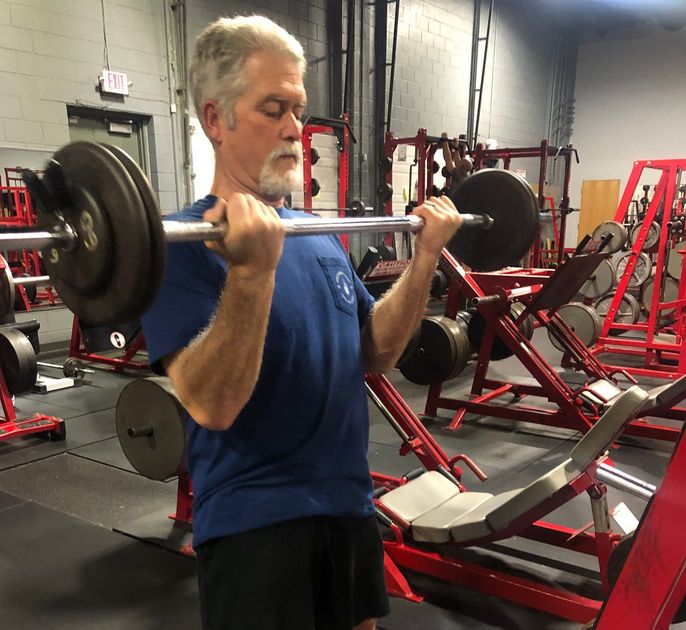 A man is lifting a barbell in a gym.