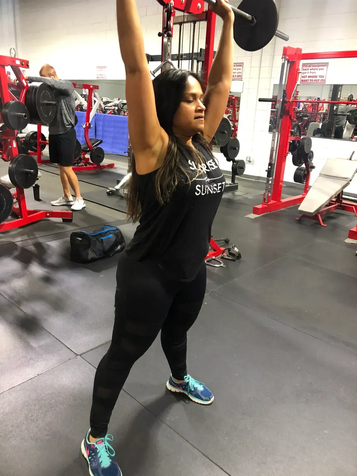 A woman is lifting a barbell over her head in a gym.