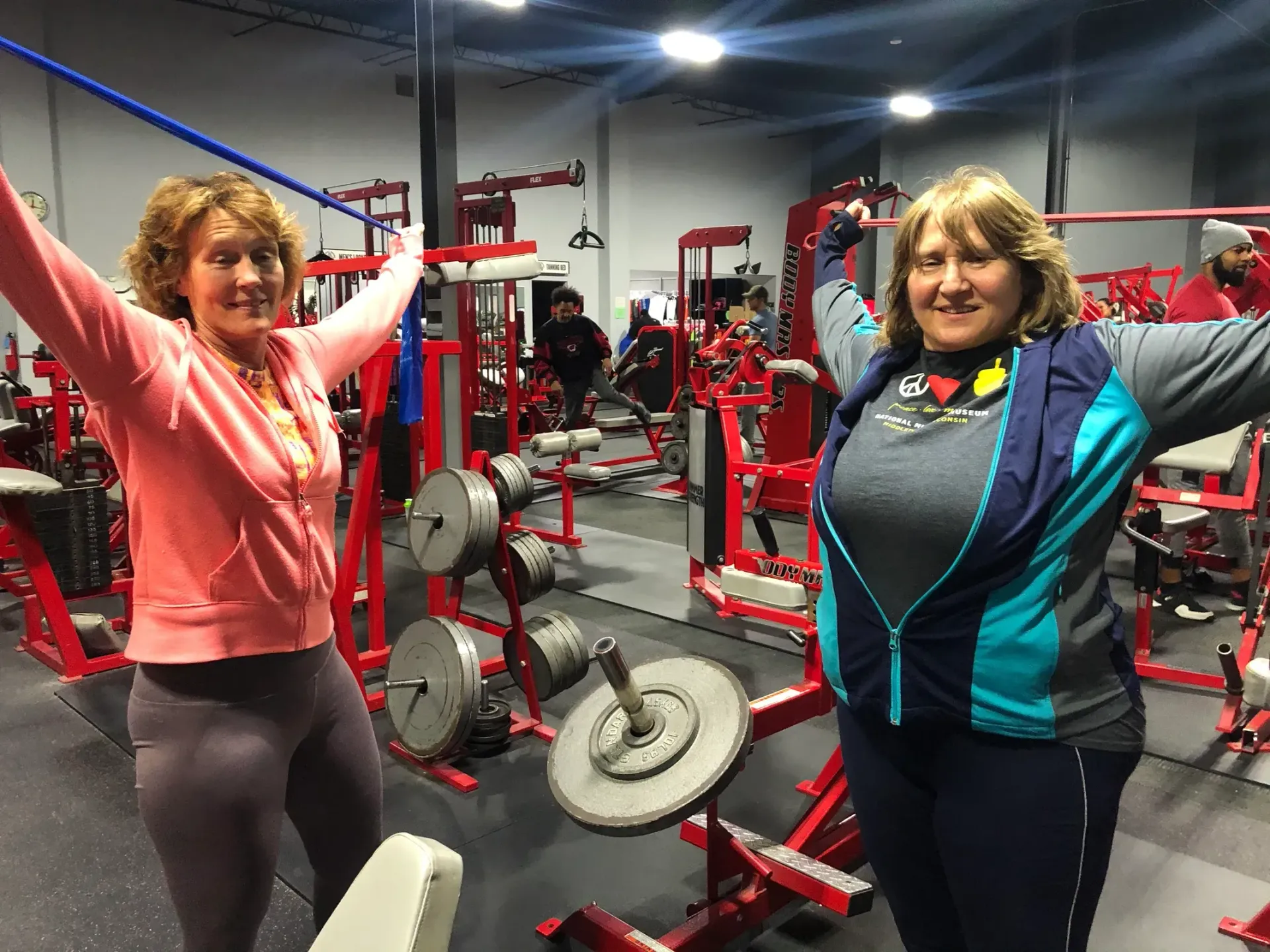Two women are standing in a gym with their arms in the air.