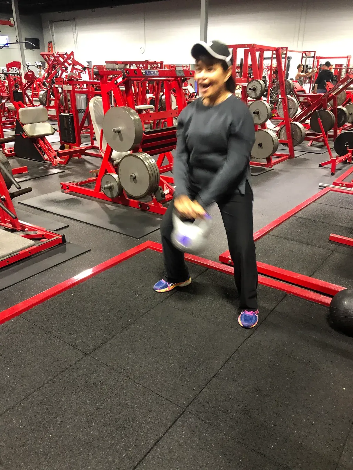 A woman is lifting a kettlebell in a gym.