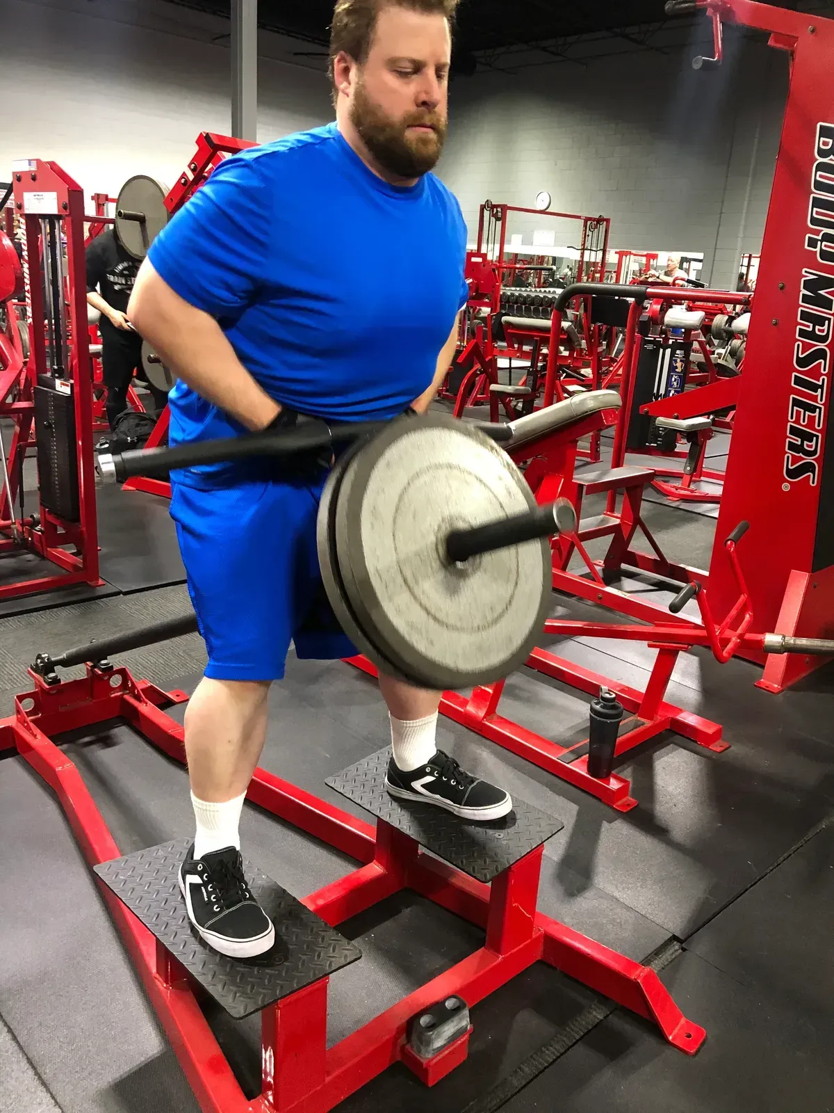 A man in a blue shirt is lifting a barbell in a gym.