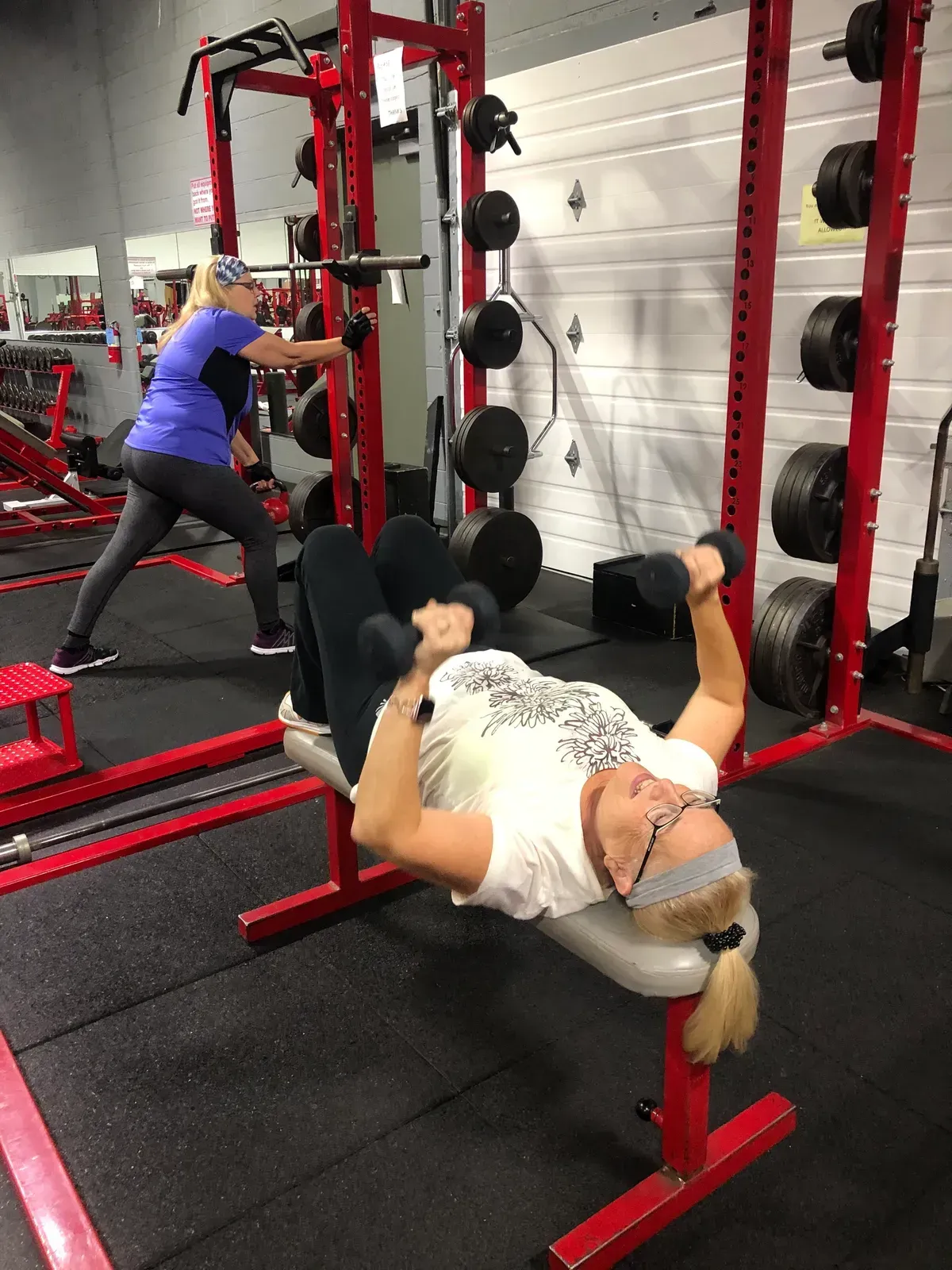 A woman is lifting a dumbbell on a bench in a gym.