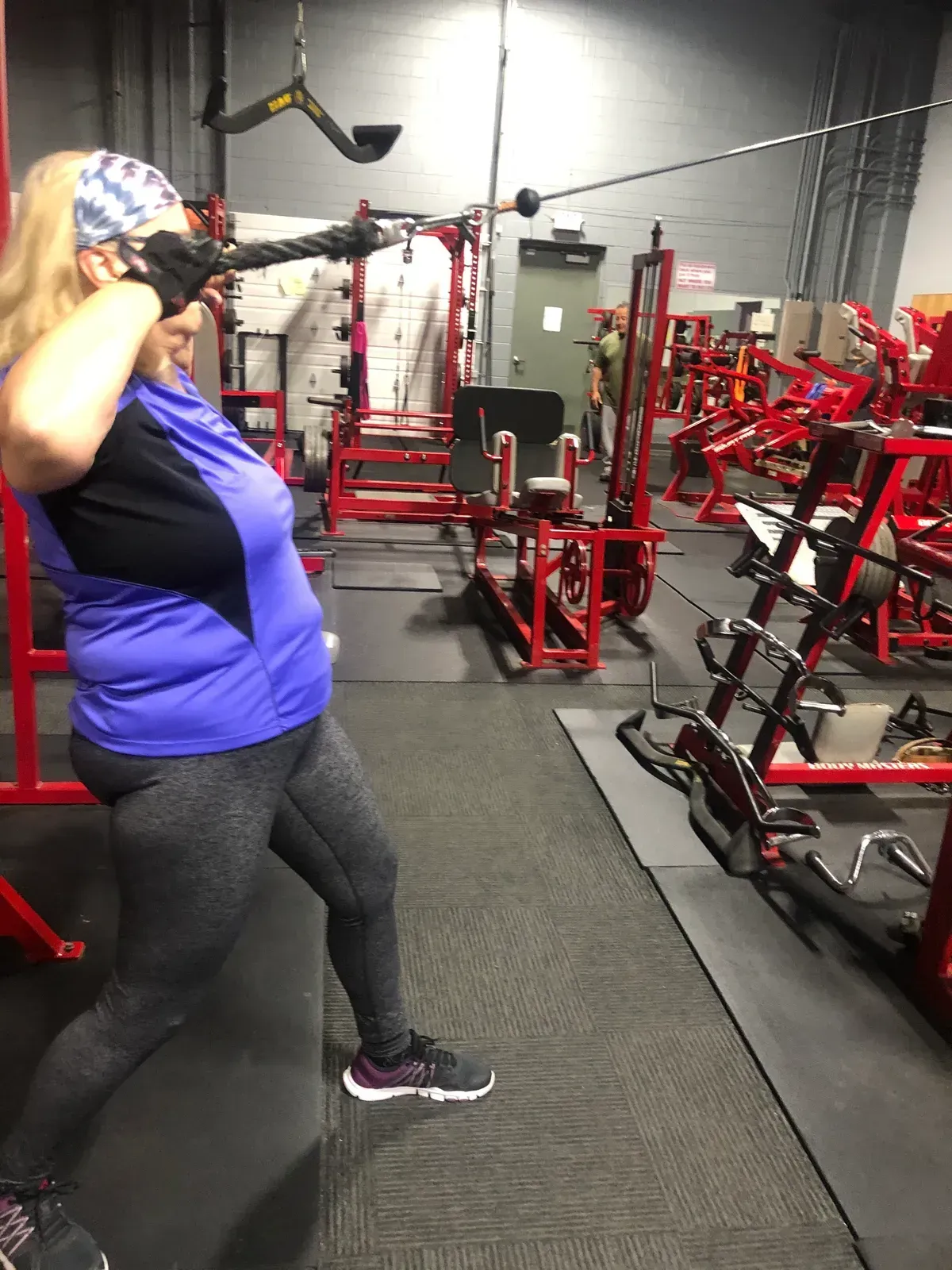 A woman is standing in a gym holding a barbell over her head.