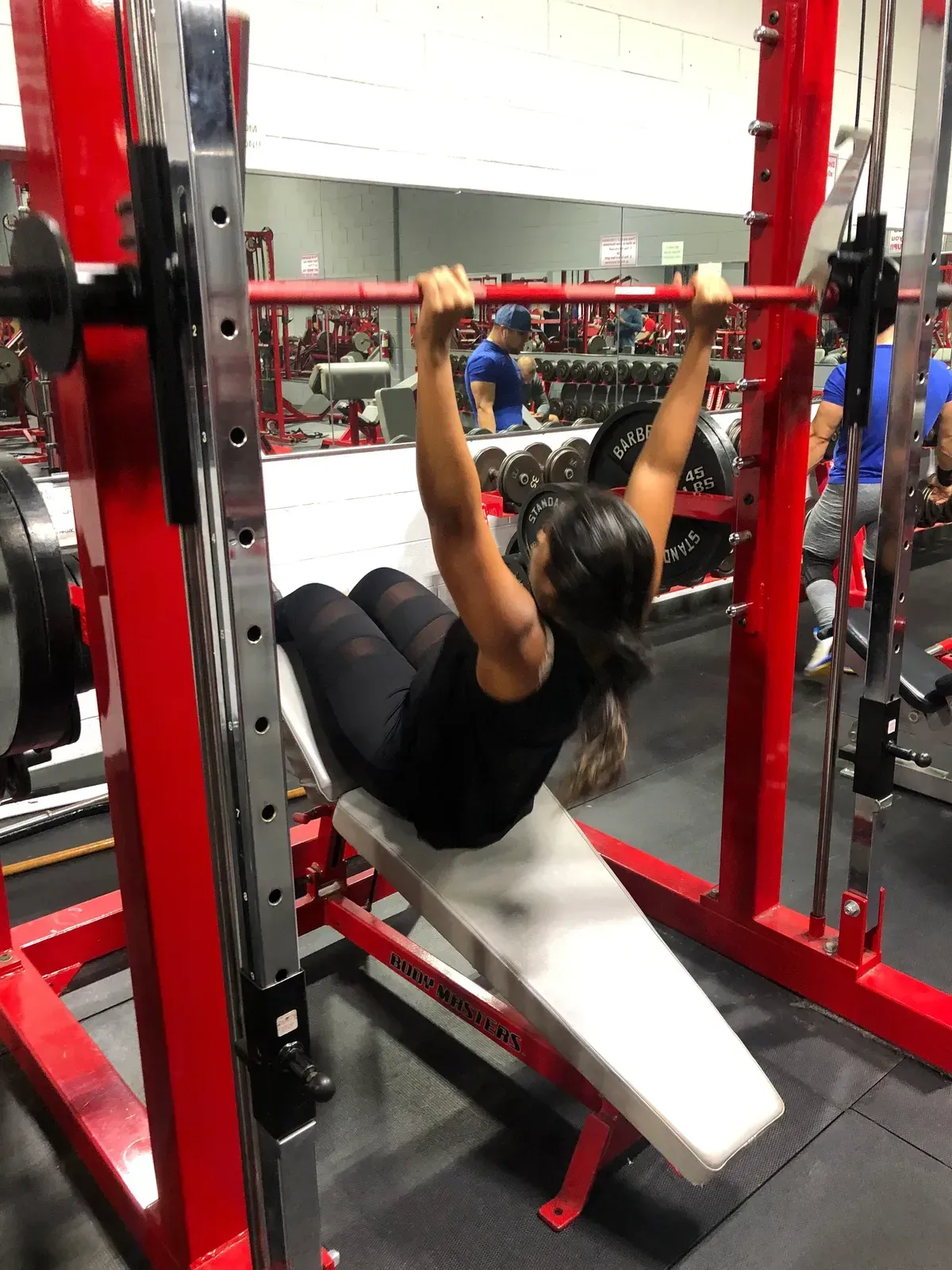 A woman is doing a pull up on a bench in a gym.