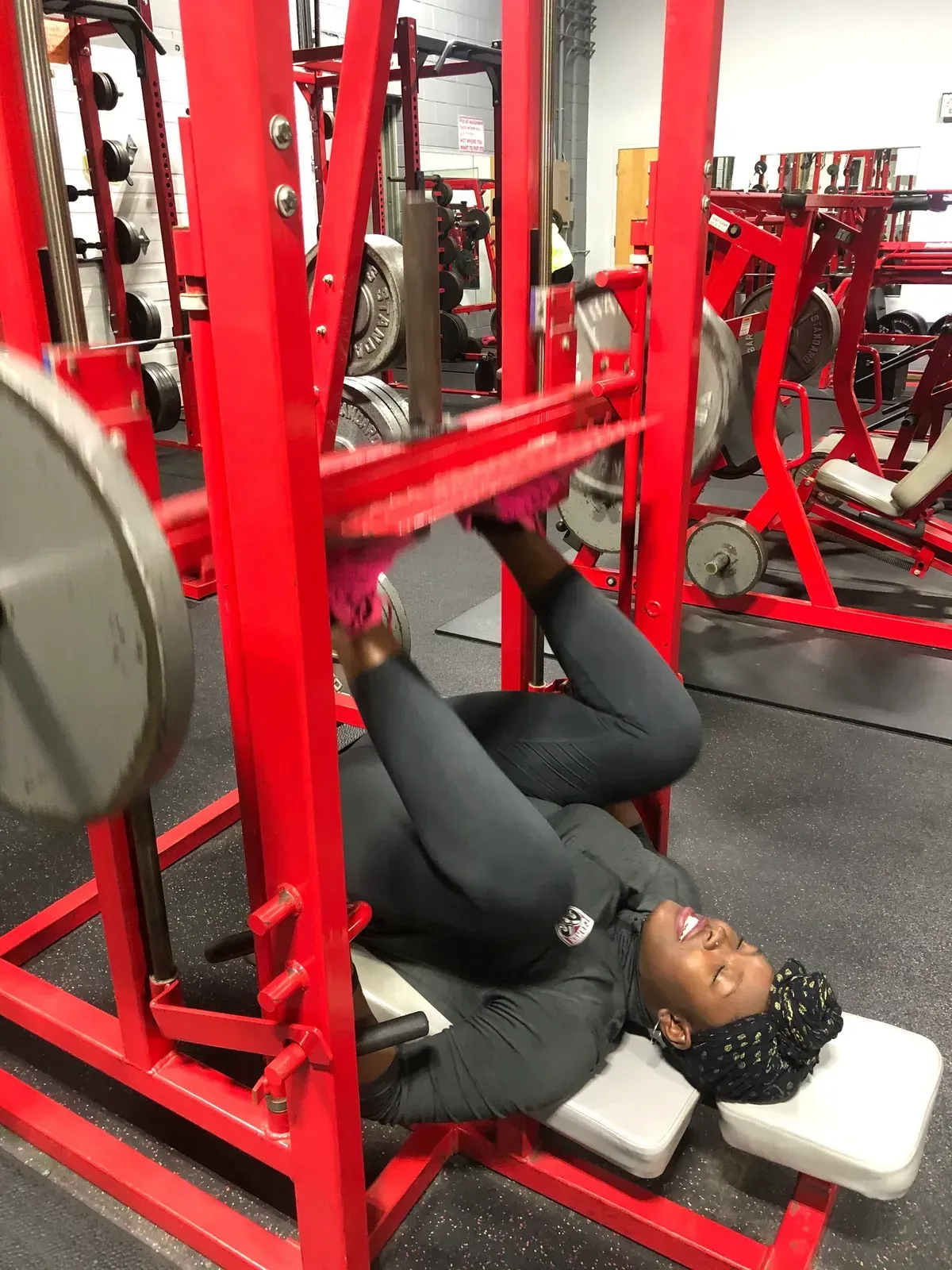 A woman is laying on a bench in a gym while lifting weights.