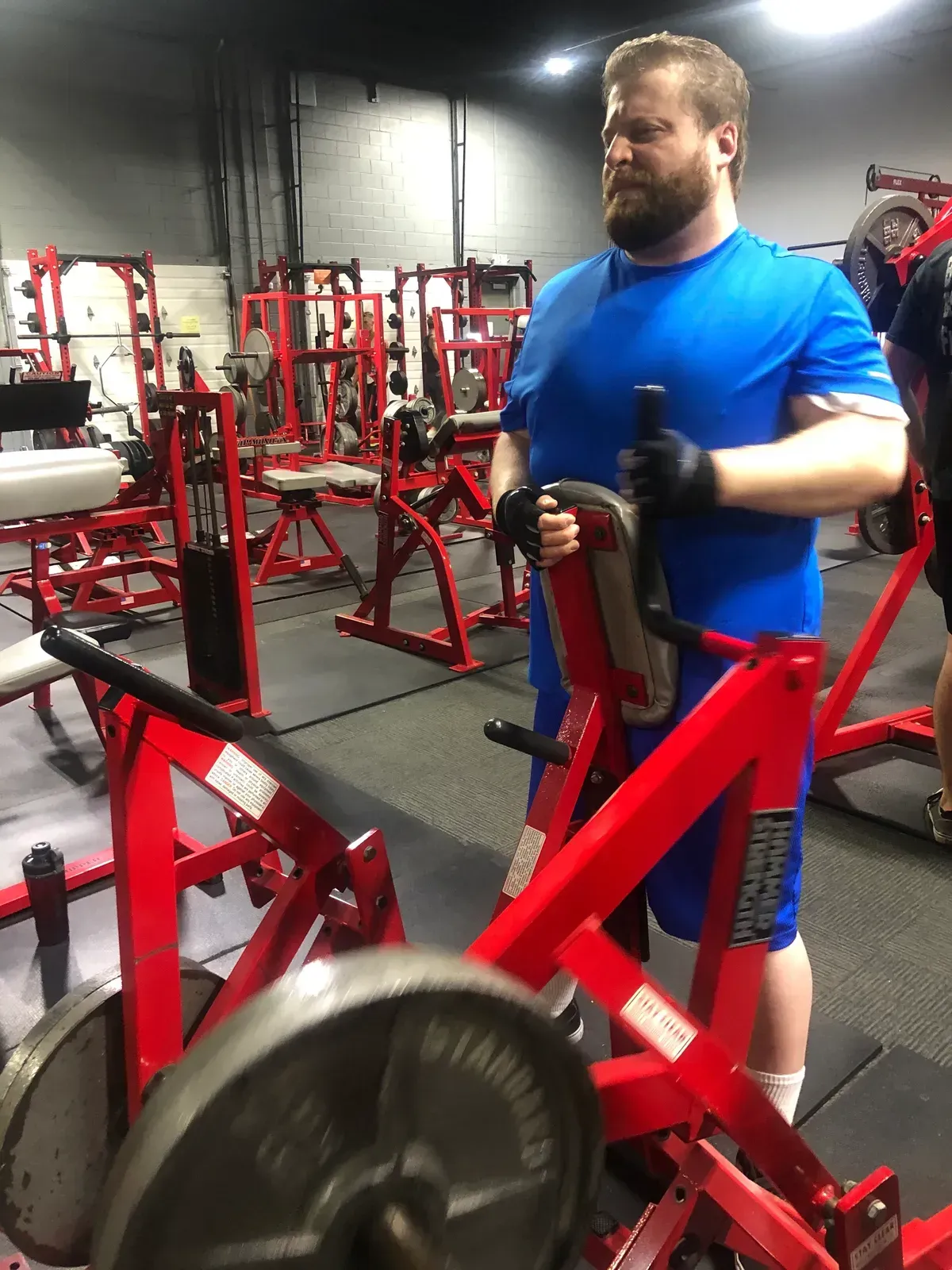 A man in a blue shirt is standing next to a red machine in a gym.