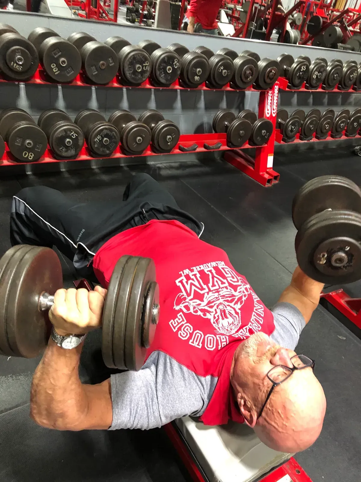 A man in a red shirt is lifting dumbbells in a gym