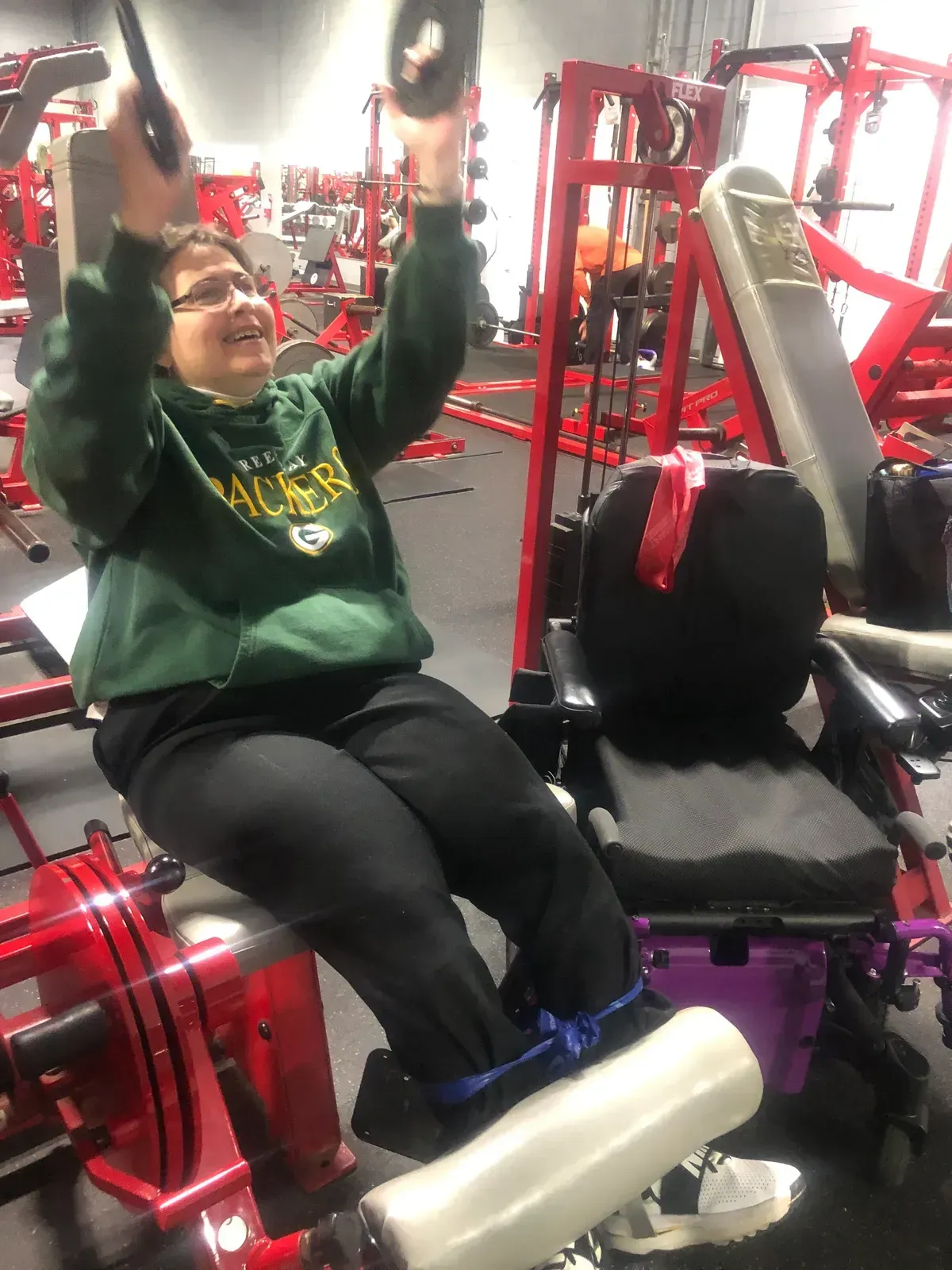 A woman in a green bay packers sweatshirt is sitting on a machine in a gym.