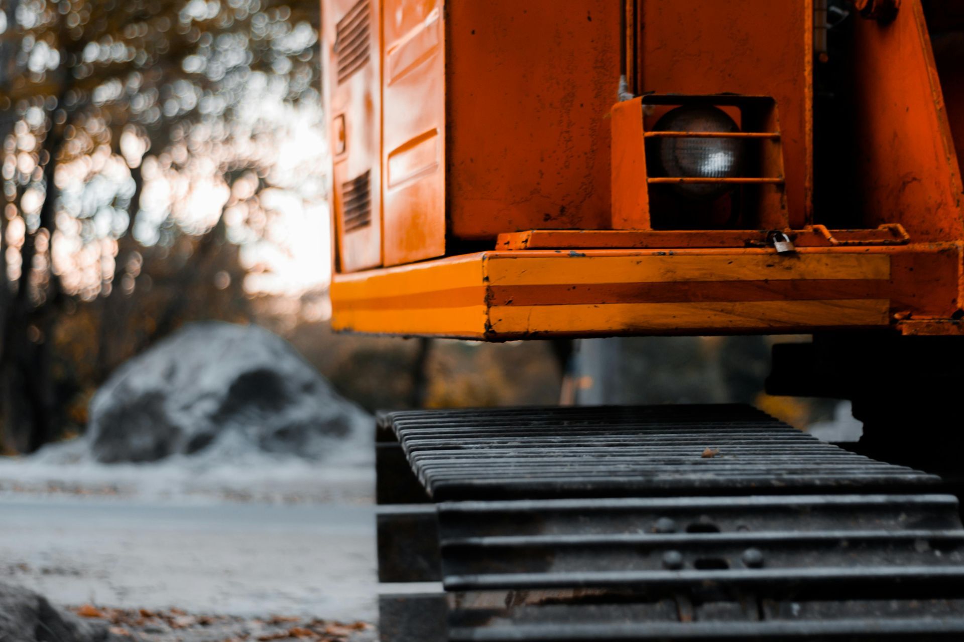 Orange construction vehicle tracks close-up, blurred background of trees and rocks.