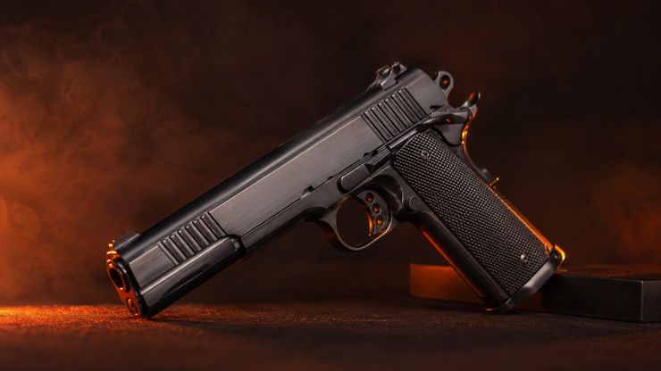 Handgun Black handgun on a dark surface with orange backlighting and smoke-like glow.