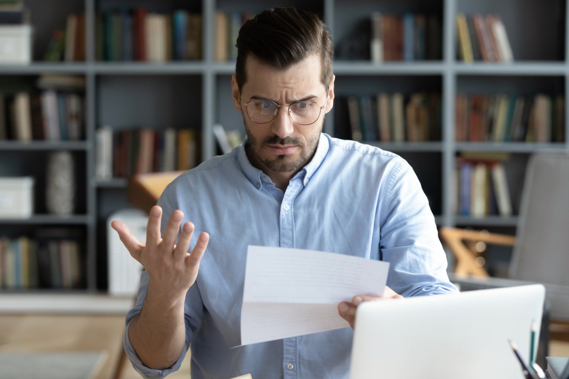 A man holding a paper in his left hand looks concerned at a problem medical bill. His right hand is gesturing frustration at the bill.