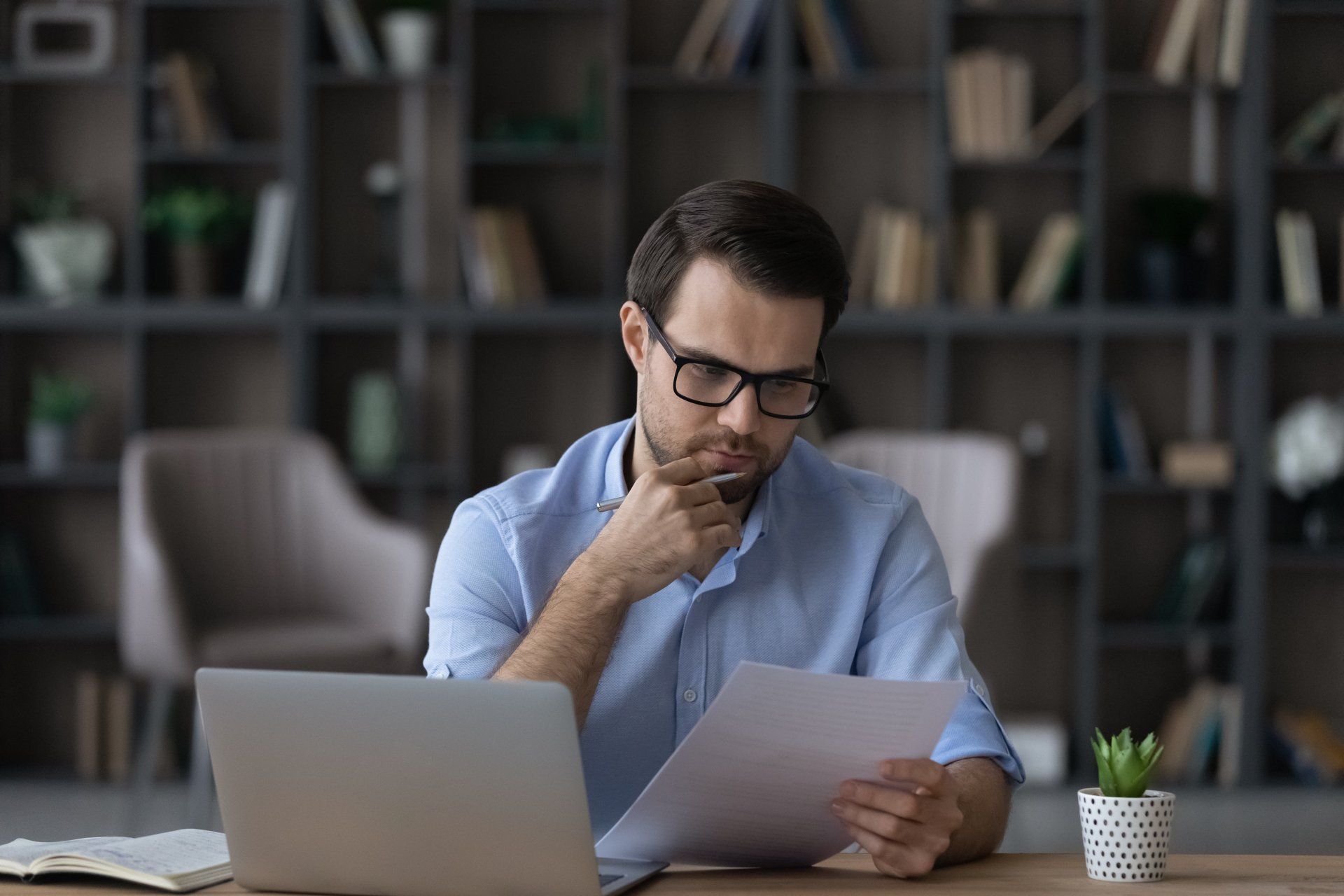 A man wearing glasses is sitting in an office looking at a problem medical bill.